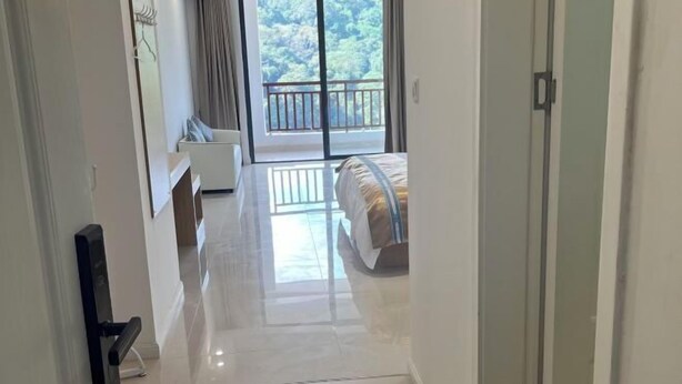 A hotel room with a bed, a sofa, a TV, and a balcony with a view of the outdoors. - Five Tigers Hotel (Boten)