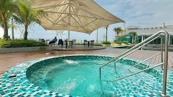A swimming pool with a tiled edge, a metal ladder, and an umbrella providing shade.