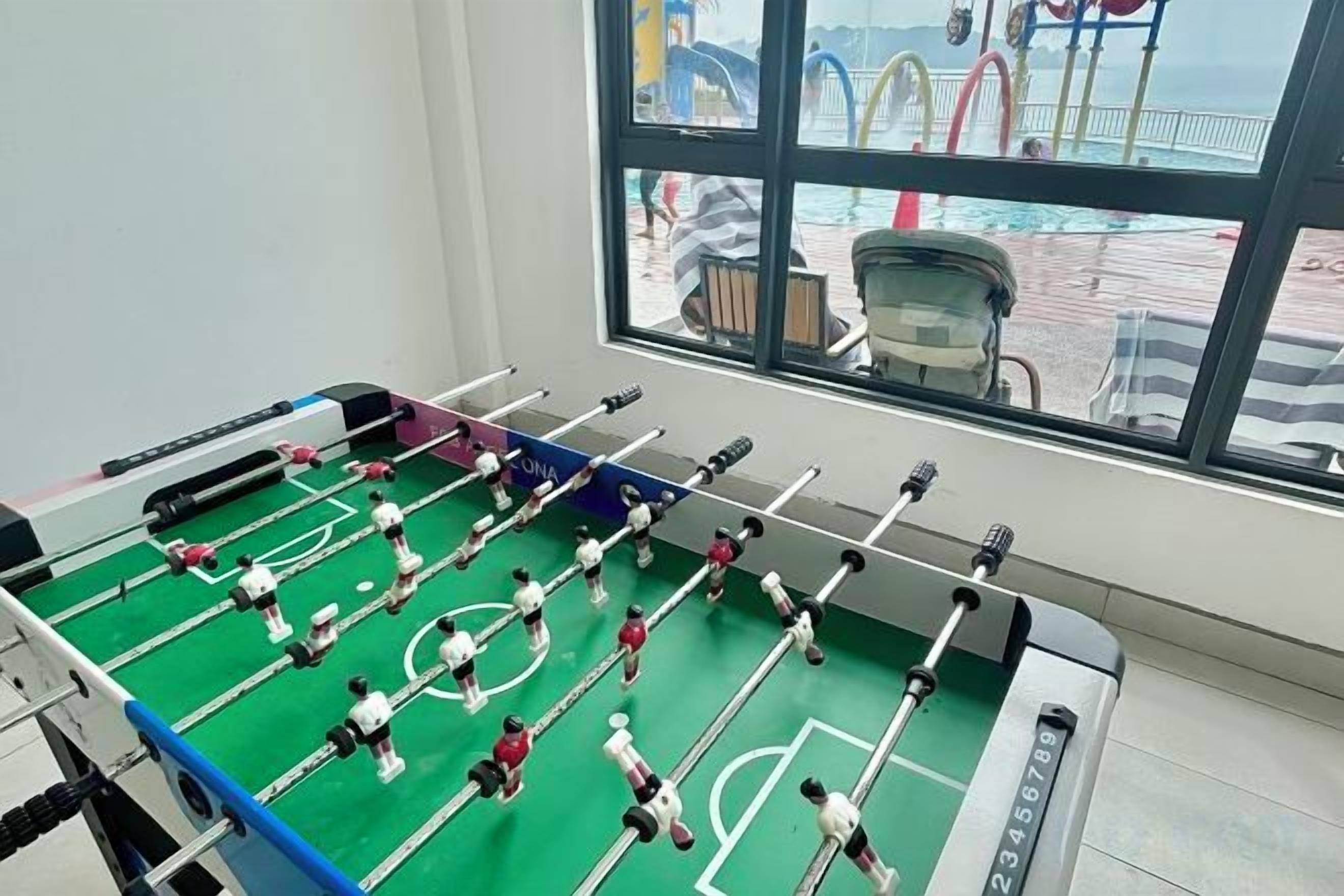 Une table de baby-foot dans une pièce dotée d’une grande fenêtre donnant sur une terrasse.