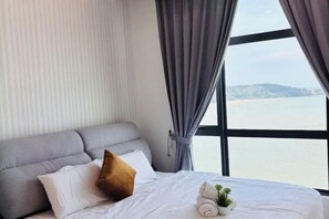 A hotel room with a bed, a grey sofa, and a view of the sea through large windows. - Imperium Residence Kuantan by Iconique (Kuantan)