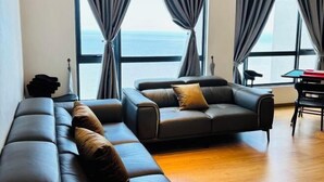 Un soggiorno moderno con divano e poltrona, ampie finestre con tende e vista sul mare.