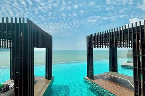 An infinity pool with a wooden deck and metal railings, overlooking a clear blue sea. - Imperium Residence Kuantan by Iconique (Kuantan)