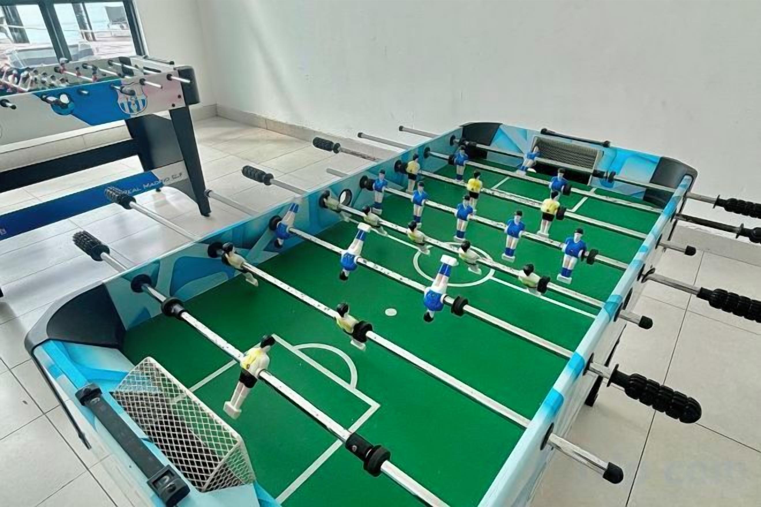 A foosball table in a room with a tiled floor and a window in the background.