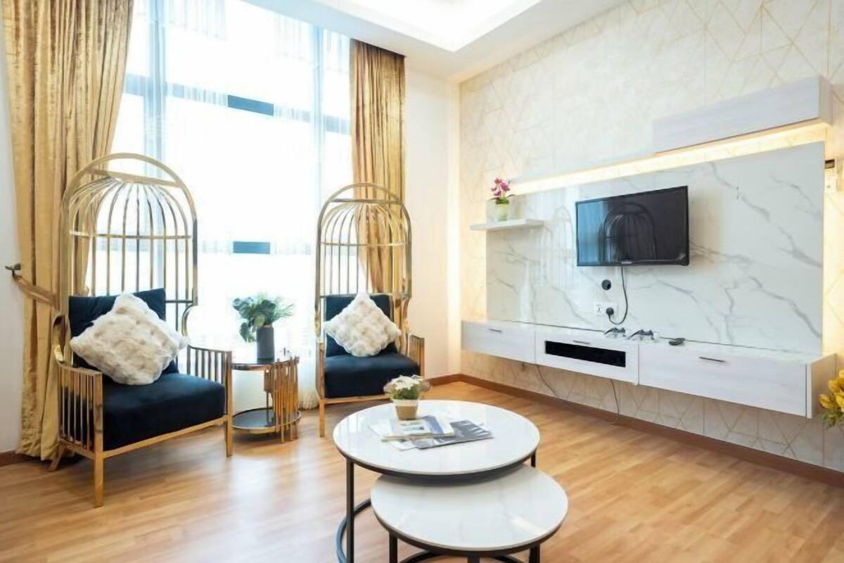 A modern living room with two wicker chairs, a round coffee table, a flat-screen TV mounted on a marble wall, and a small side table with a plant.