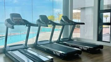 Three treadmills in a room with large windows overlooking a swimming pool.