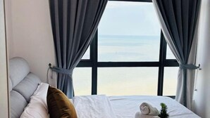 Una camera d'albergo con una grande finestra, un letto con lenzuola bianche, un cuscino marrone e una piccola pianta in vaso.