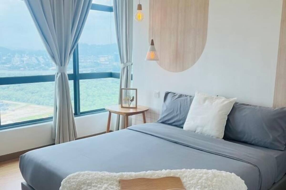 A modern bedroom with a large bed, a view of the city, and a small table with a lamp.