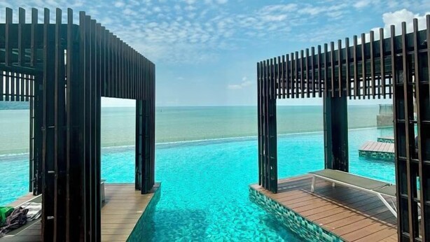 Una piscina a sfioro con terrazza in legno e ringhiere in metallo, con vista sul mare turchese.
