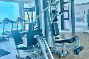 A gym with exercise equipment, a treadmill, and a large window with a view. - Imperium Residence Kuantan by Iconique (Kuantan)