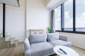 A modern living room with a grey sofa, a small round table, and a view of the city through large windows. - Bangkok Sukhumvit 87 Boutique Apartment (Bangkok)