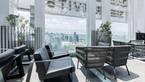 A modern rooftop lounge with black leather sofas and wicker chairs, offering panoramic city views.