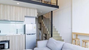 A modern kitchen with a built-in oven, a refrigerator, and a microwave. There is a staircase leading to an upper level.