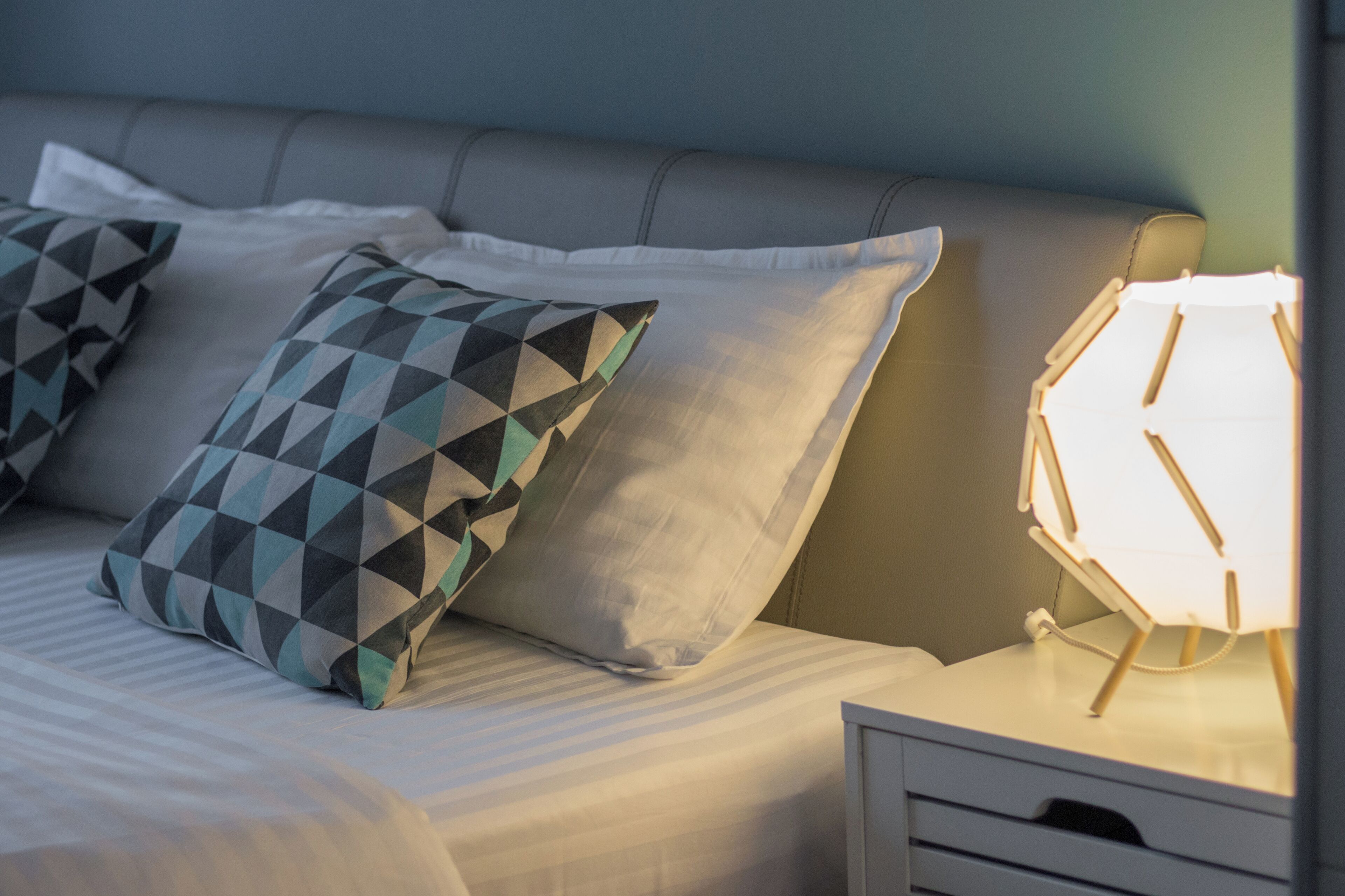 Una cama bien hecha con almohadillas estampadas y una lámpara de noche.