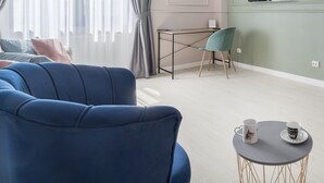 Un salon moderne avec un canapé bleu, une petite table ronde sur laquelle reposent deux tasses, un bureau avec une chaise et un téléviseur affichant le logo de Netflix.