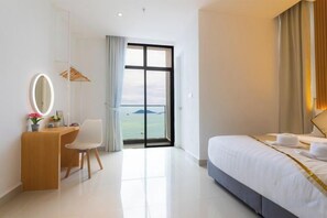 Ein Hotelzimmer mit einem Bett, einem Schreibtisch mit Stuhl, einem Spiegel und Blick ins Freie durch ein großes Fenster.