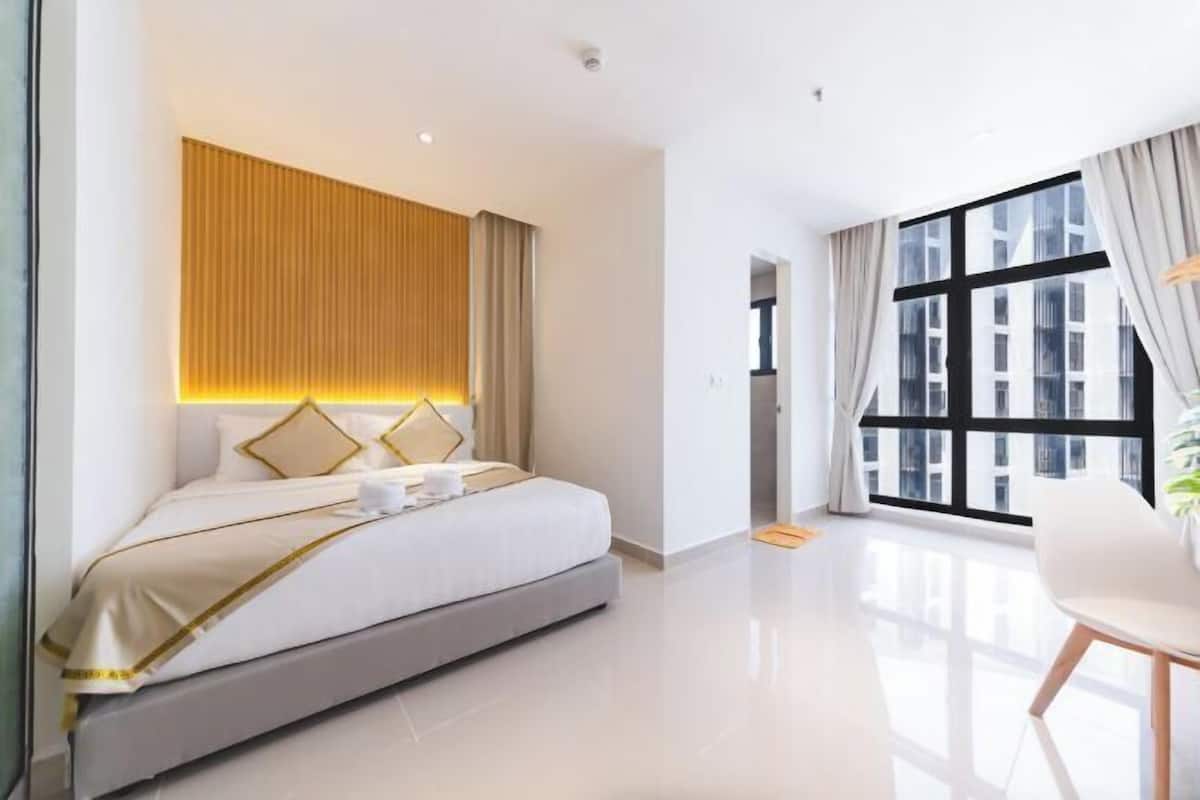 Une chambre d’hôtel moderne avec un grand lit, une table de chevet, une fenêtre avec des rideaux et une vue sur les immeubles.