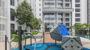 Un espace de remise en forme en plein air, équipé d’appareils d’exercice, entouré d’un bâtiment moderne doté de balcons et d’une piscine.