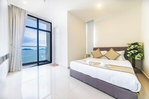 A modern hotel room with a large bed, a view of the sea, and a balcony with curtains.
