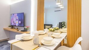 Un comedor moderno con una larga mesa dispuesta para una comida, un televisor en la pared y un espejo que refleja la habitación.