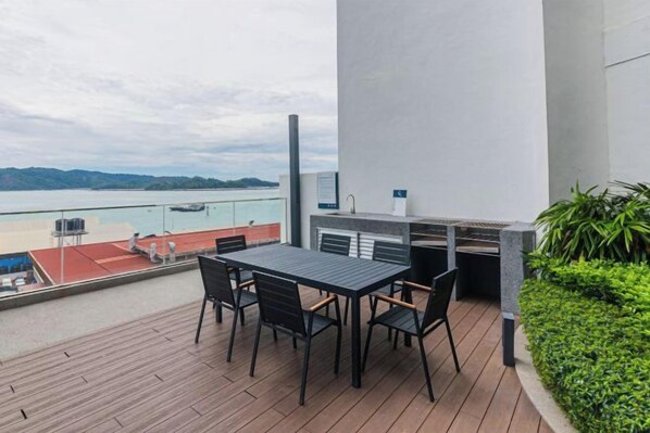 A balcony with a table and chairs, overlooking a body of water and a red-roofed building. - 5StarPanda Seaview at The Shore Kota Kinabalu (Kota Kinabalu)