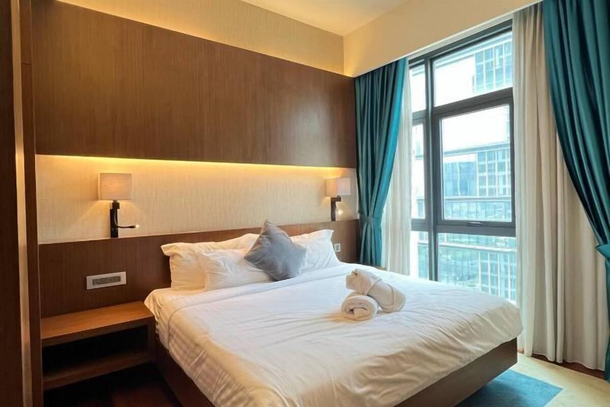 Een hotelkamer met een groot bed, twee bedlampjes, een nachtkastje en een raam met gordijnen.
