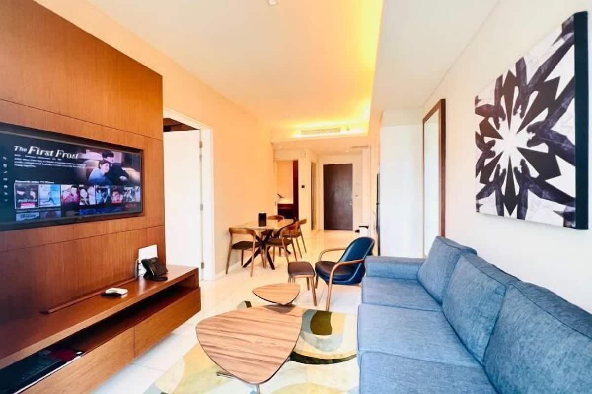 Een moderne woonkamer met een flatscreen televisie, een blauwe bank, een bijzettafeltje en een eethoek met stoelen en een tafel.