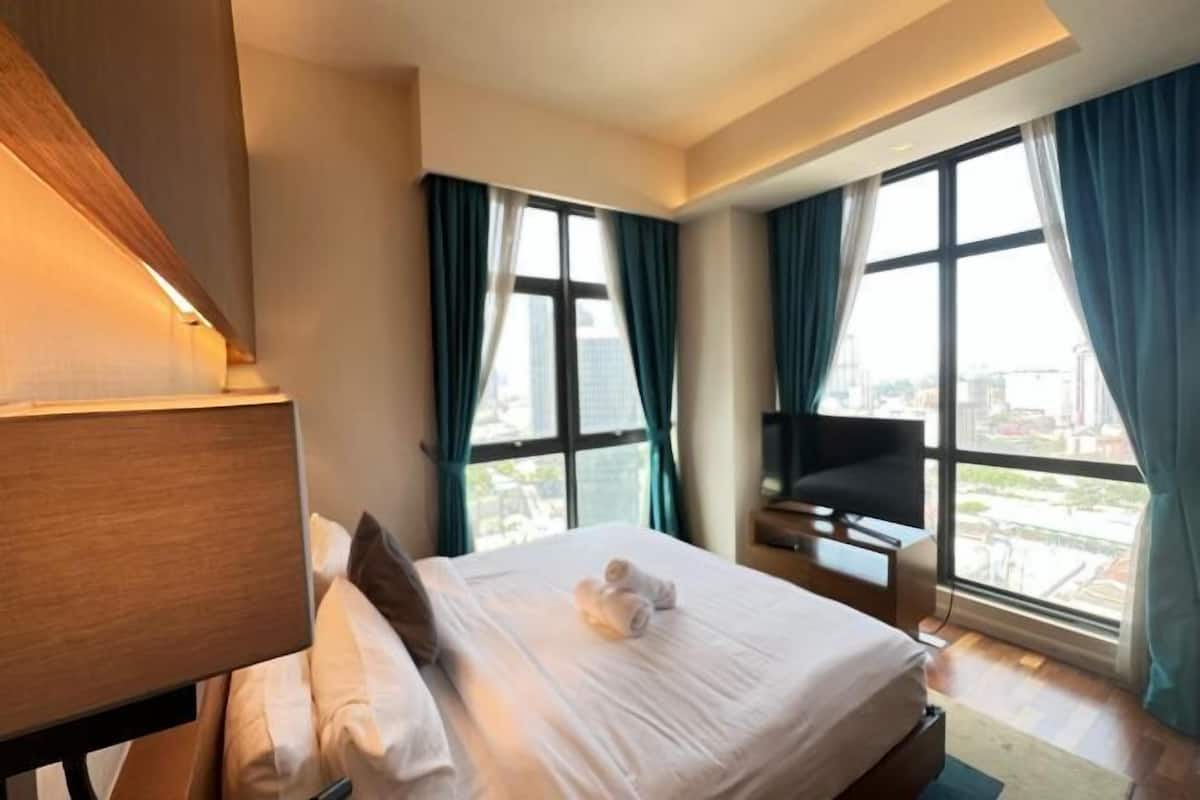 Een hotelkamer met een bed, een televisie en grote ramen met gordijnen.