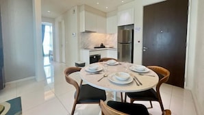 A modern dining area with a round table set for four, a kitchen in the background, and a large dark door. - Tribeca Homestay Bukit Bintang TRX (Kuala Lumpur)