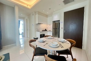 Un espace repas moderne avec une table ronde dressée pour quatre personnes, une cuisine en arrière-plan et une grande porte sombre.