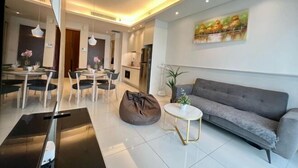 A modern living room with a grey sofa, a dining area with a table and chairs, and a kitchen in the background. - Tribeca Homestay Bukit Bintang TRX (Kuala Lumpur)