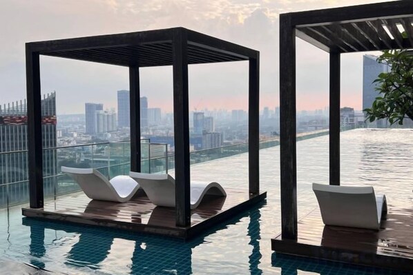 Piscina infinita en la azotea con sillones de descanso y vista a la ciudad.