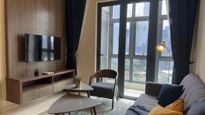 A modern living room with a flat-screen TV, a sofa, a chair, a small table, and a large window offering a city view. - Tribeca Homestay Bukit Bintang TRX (Kuala Lumpur)