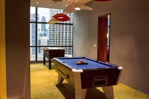 Una mesa de billar en una habitación con vistas a un paisaje urbano a través de amplios ventanales.