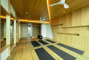 Une pièce spacieuse dotée d’un plancher en bois, de tapis de sol noirs pour la pratique d’exercices et de ventilateurs de plafond.