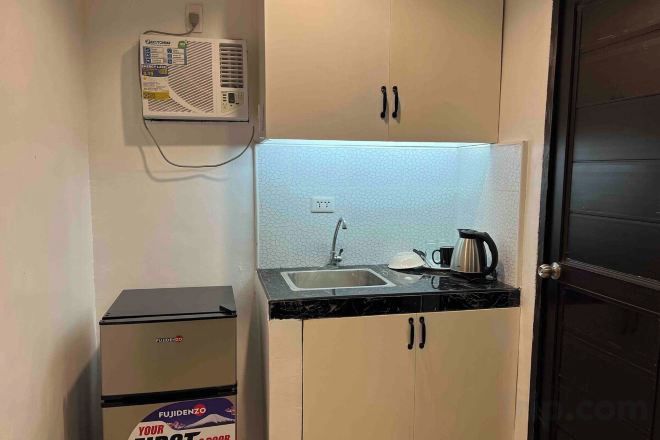 Una cocina compacta con un lavamanos empotrado, un refrigerador pequeño y un equipo de aire acondicionado montado en la pared.