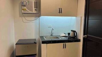 Una cocina compacta con un lavamanos empotrado, un refrigerador pequeño y un equipo de aire acondicionado montado en la pared.