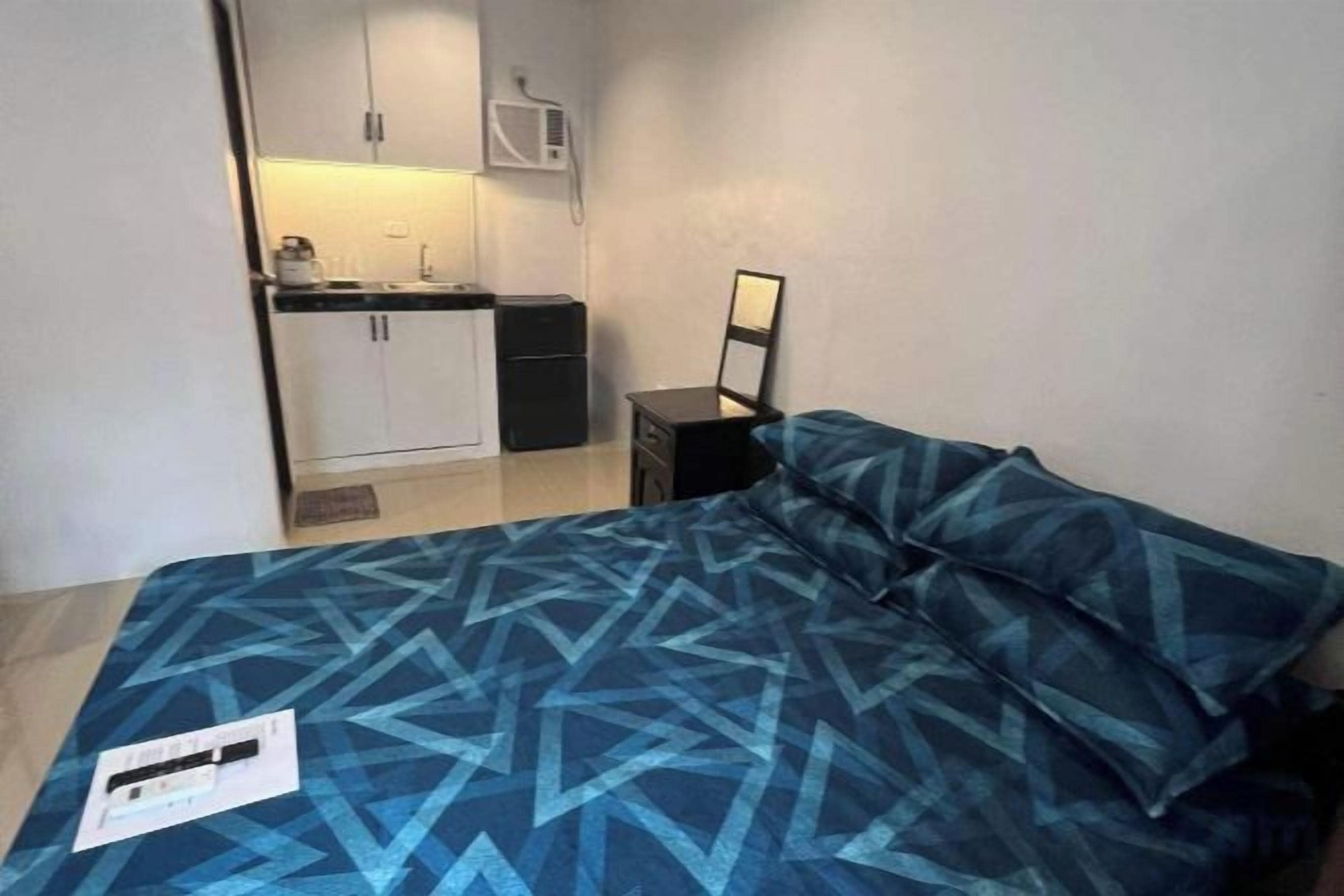 Un dormitorio con cama, mesita de noche, espejo y vistas a una kitchenette.