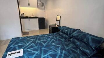 Un dormitorio con cama, mesita de noche, espejo y vistas a una kitchenette.