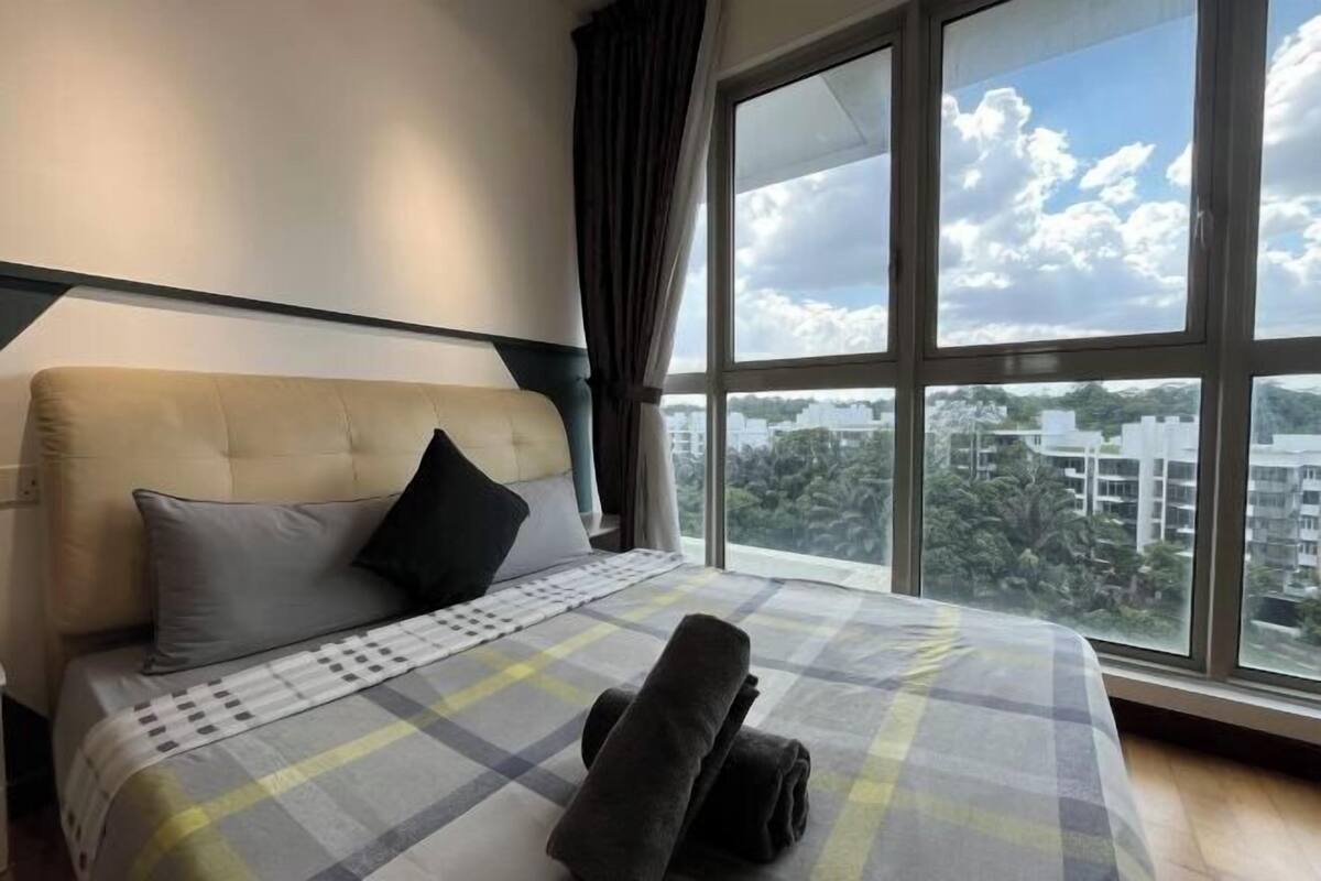 A hotel room with a bed, a window with a city view, and a window blind.