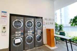 A laundry area with four washing machines, a bench, and a trash bin. - Homestay near to PWTC @ BY AWESOMESTAY (Kuala Lumpur)