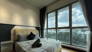 A bedroom with a large window, a bed with a plaid bedspread, a nightstand, and a headboard. - Homestay near to PWTC @ BY AWESOMESTAY (Kuala Lumpur)