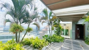 A rooftop garden with palm trees and various plants, a stone pathway, and a view of the cityscape. - Homestay near to PWTC @ BY AWESOMESTAY (Kuala Lumpur)