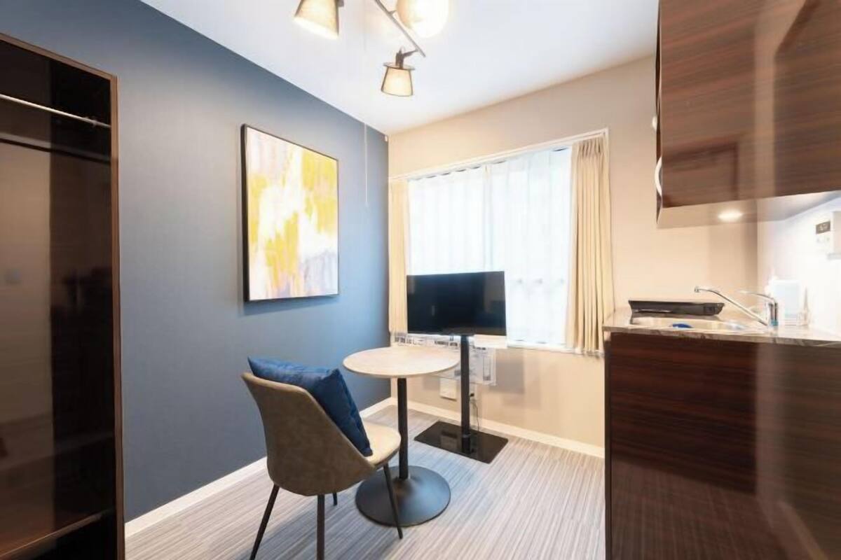 Una habitación pequeña con una mesa de comedor, una silla, un televisor y un ventanal con cortinas.