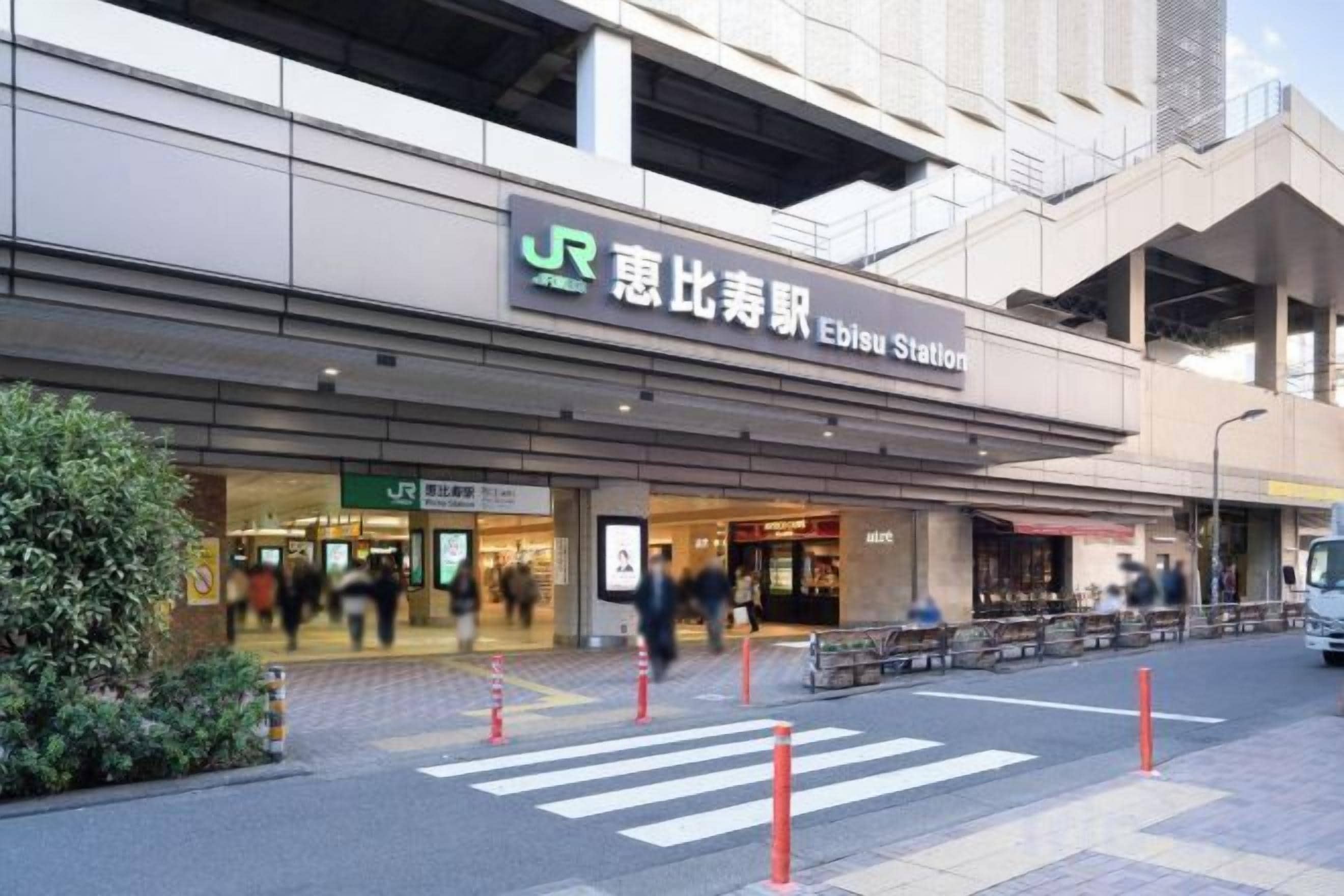 Ein Gebäude mit einem Schild, auf dem 'Ebisu Station' steht, und einer Fußgängerampel davor.