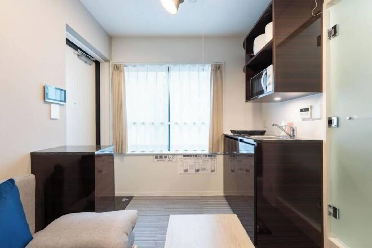 Un espacio habitable compacto con kitchenette, sofá, mesa de comedor y ventana con cortinas.