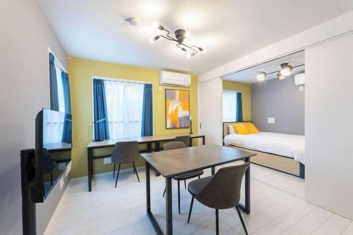 Habitación pequeña con cama, escritorio, sillas, televisor y ventana.
