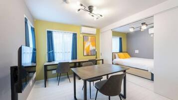 A compact room with a bed, a desk, chairs, a TV, and a window.