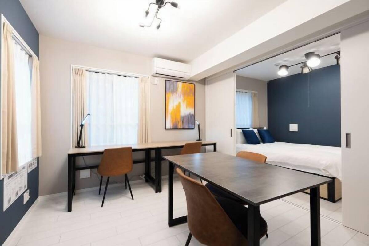 Una habitación de hotel moderna con zona de comedor, cama y un ventanal grande.