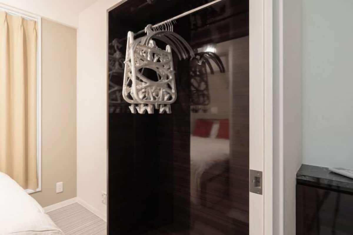 Habitación de hotel con cama, puerta con perchero y espejo que refleja parte de la habitación.