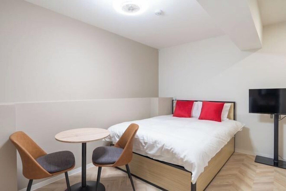 A hotel room with a bed, two chairs, a small table, and a TV.